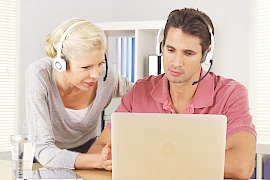 Ein Mann und eine Frau sitzen vor dem PC, haben Headsets und kommunizieren mit jemandem online. So kann die Ausbildung in Traumdeutung erfolgen.