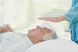 Mann bekommt Heilbehandlung mit Handauflegen im Liegen.