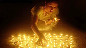Eine Hindufrau zündet nachts viele Kerzen im Freien an. Ein symbolischer Ausdruck für das Leben, das eine alte Seele führt.